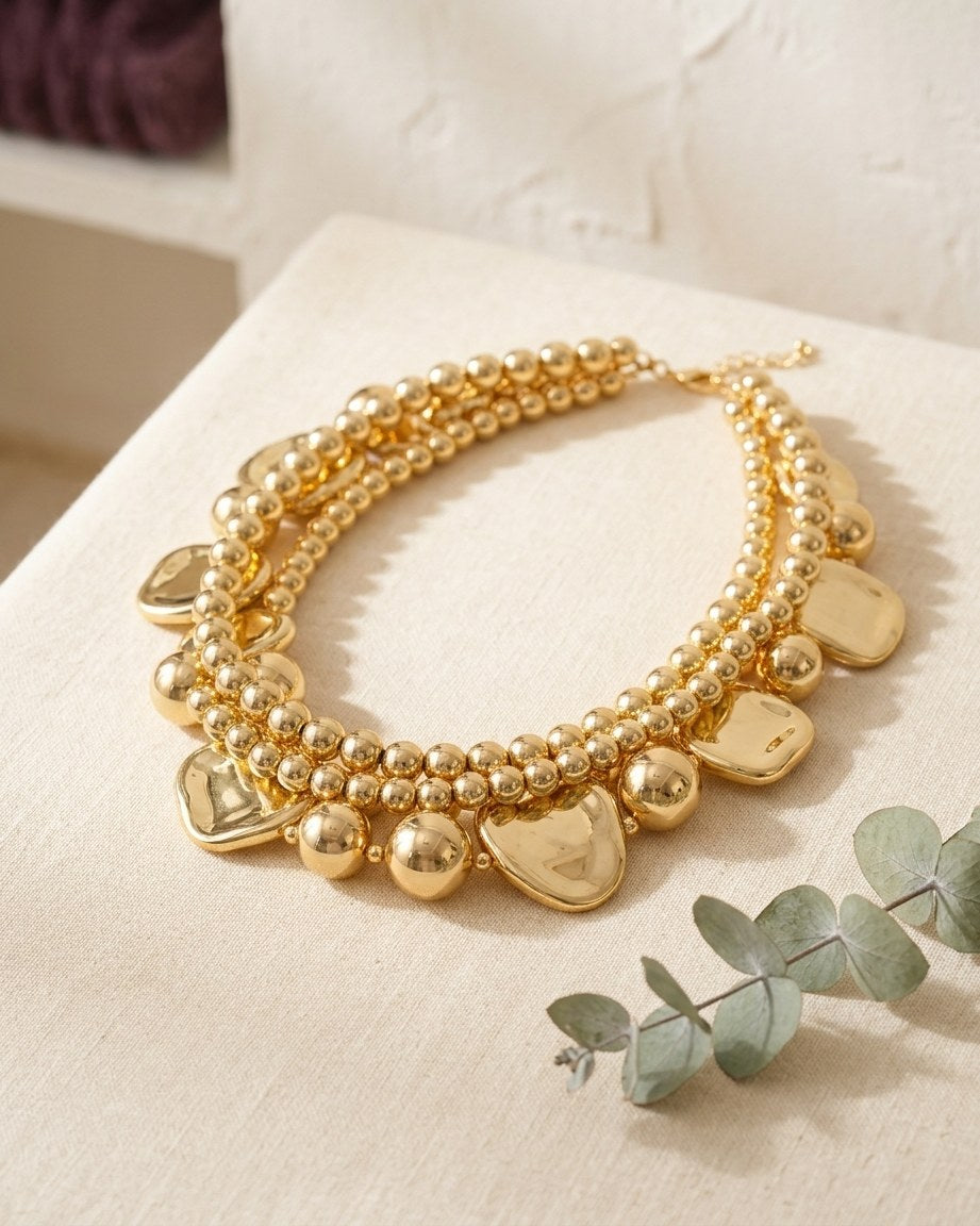 Gold-tone beaded heart choker on a cream linen table