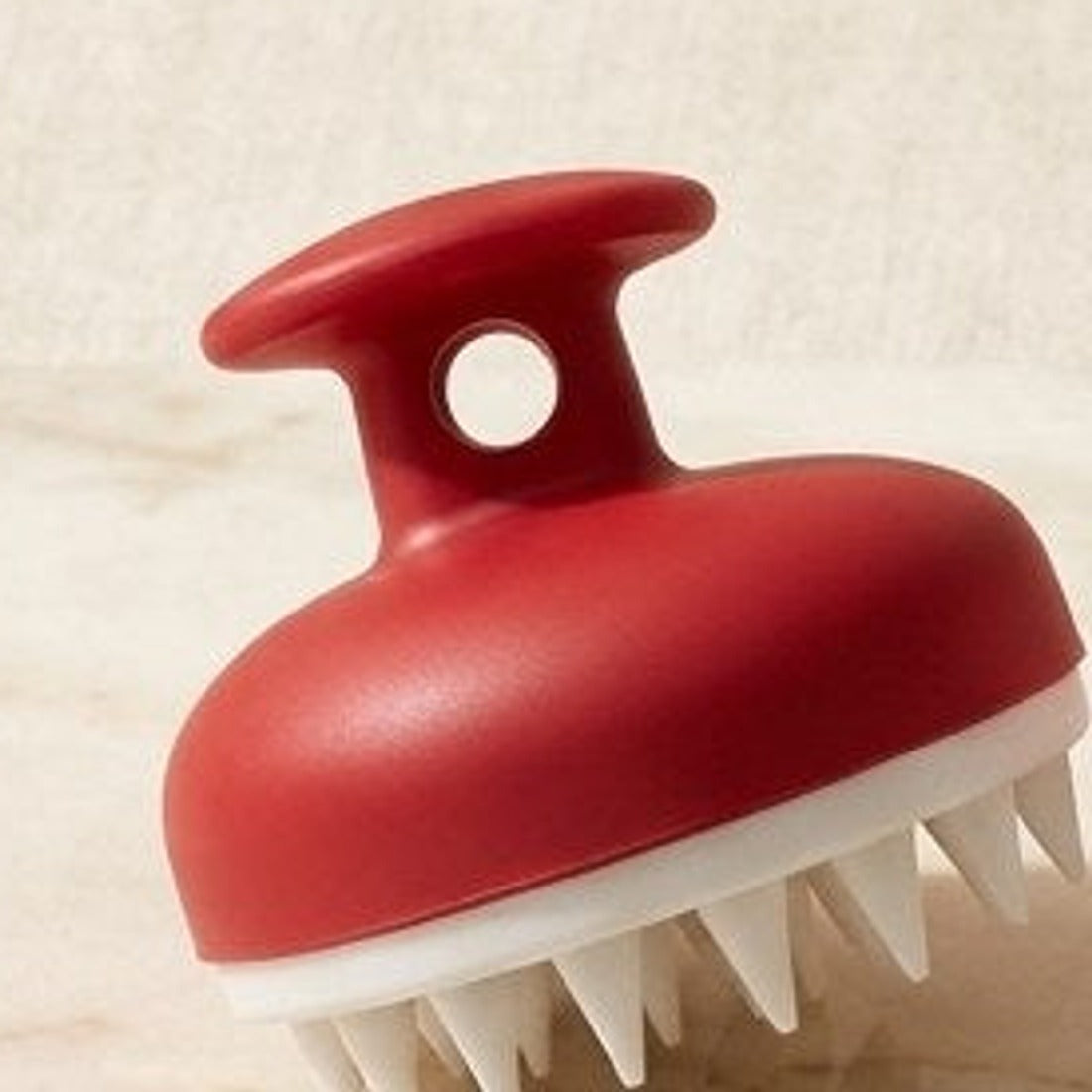 Red silicone scalp massage brush on a cream background